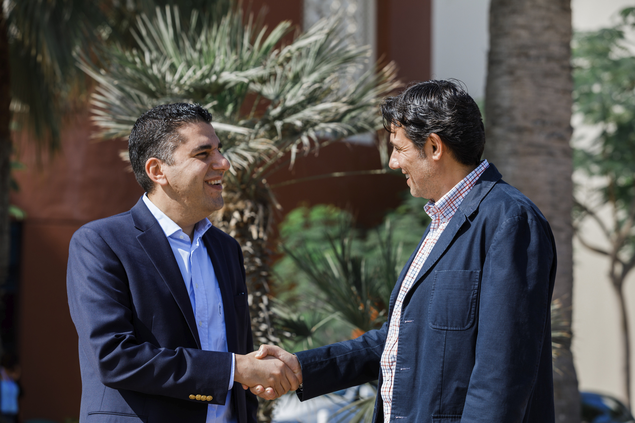 Two men in suits standing outside shaking hands.