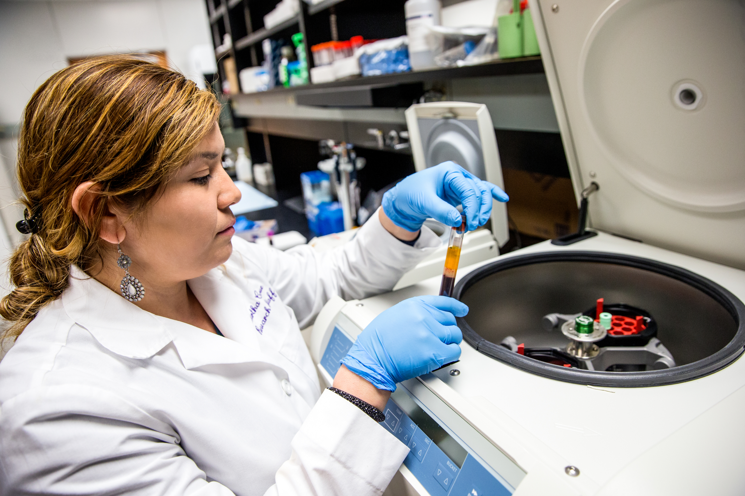 Female technician wearing lab coat and gloves places vial of blood in testing machine in medical laboratory of Chicago hospital.