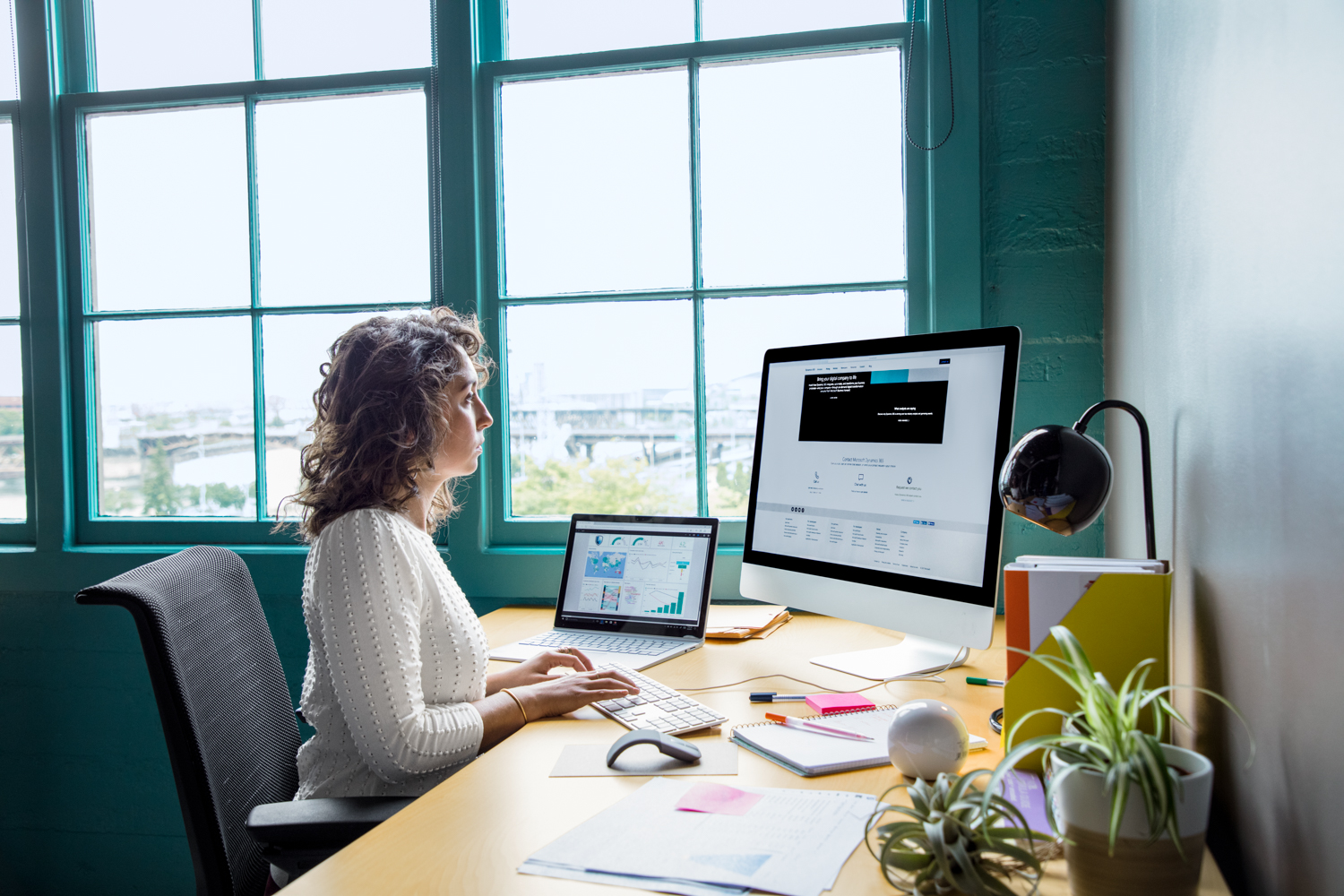 Office worker sitting at desk using an all-in-one computer in casual office with a laptop also on desk.