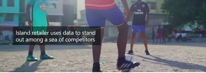 Three teenagers playing soccer in a dirt field. There are apartment buildings and other people in the background. 