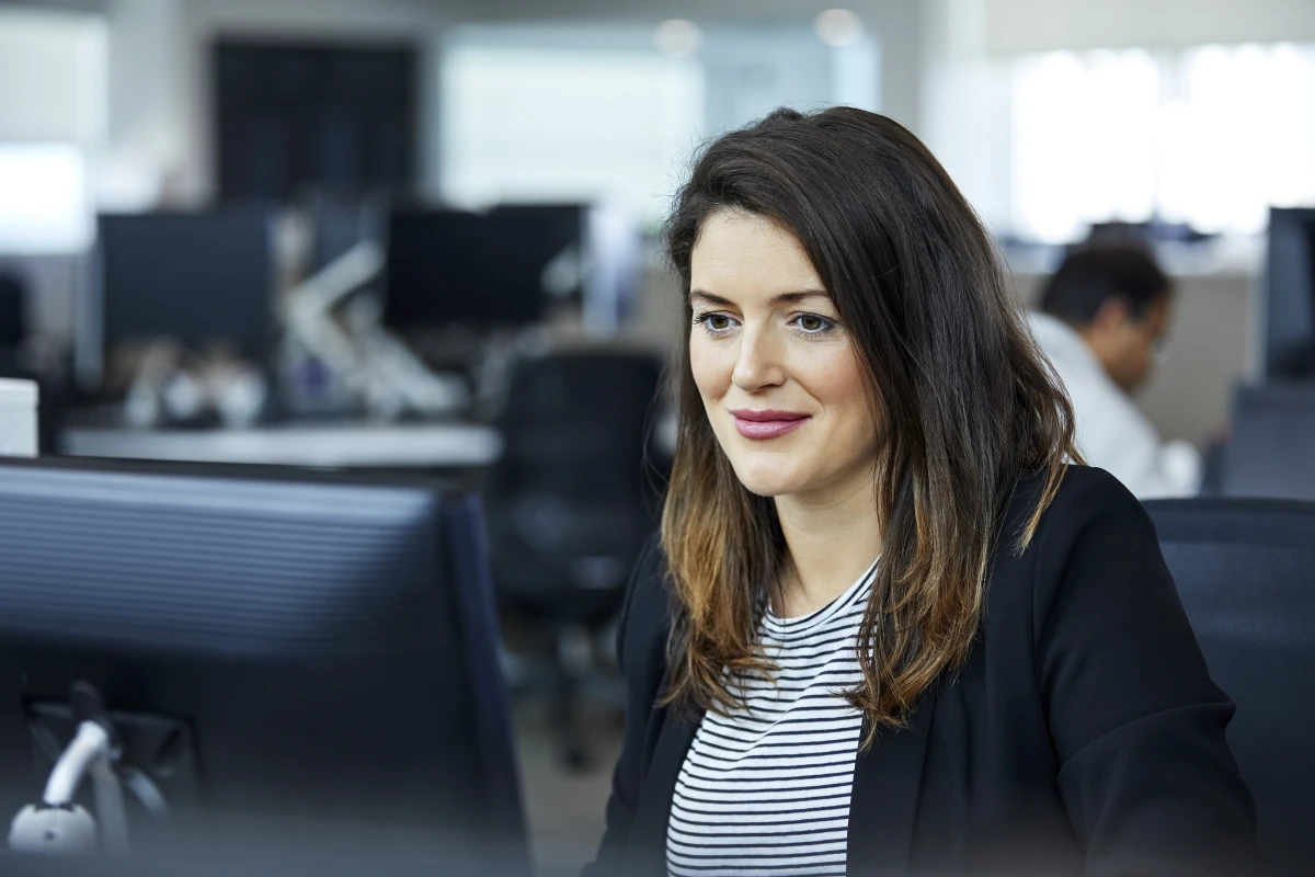 Smiling business woman using a computer, sitting at a desk in an office.