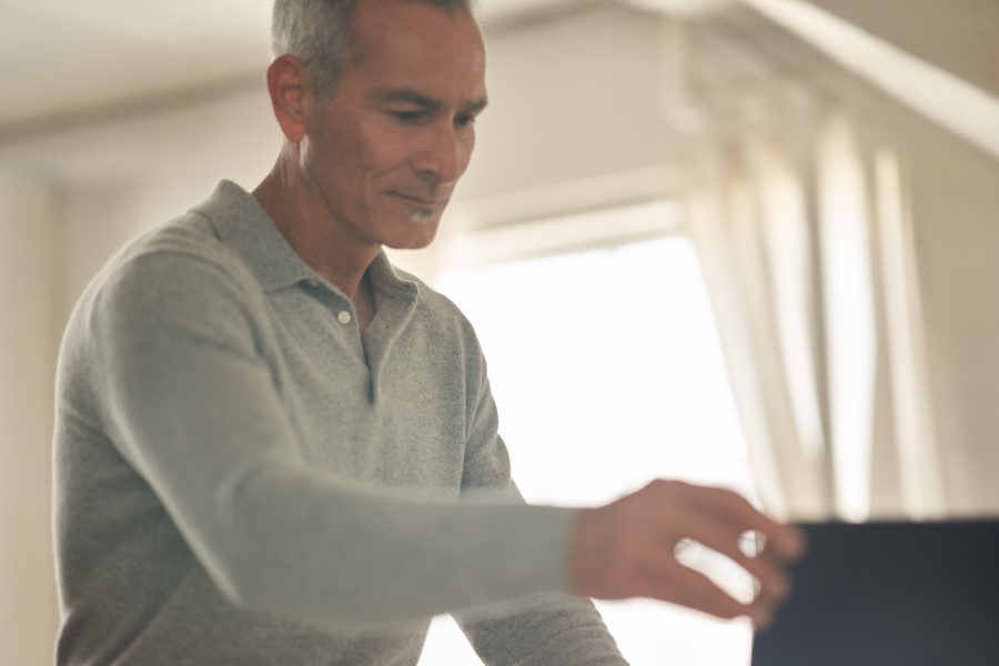 A man using a laptop with his hand outreached to the top of the screen.