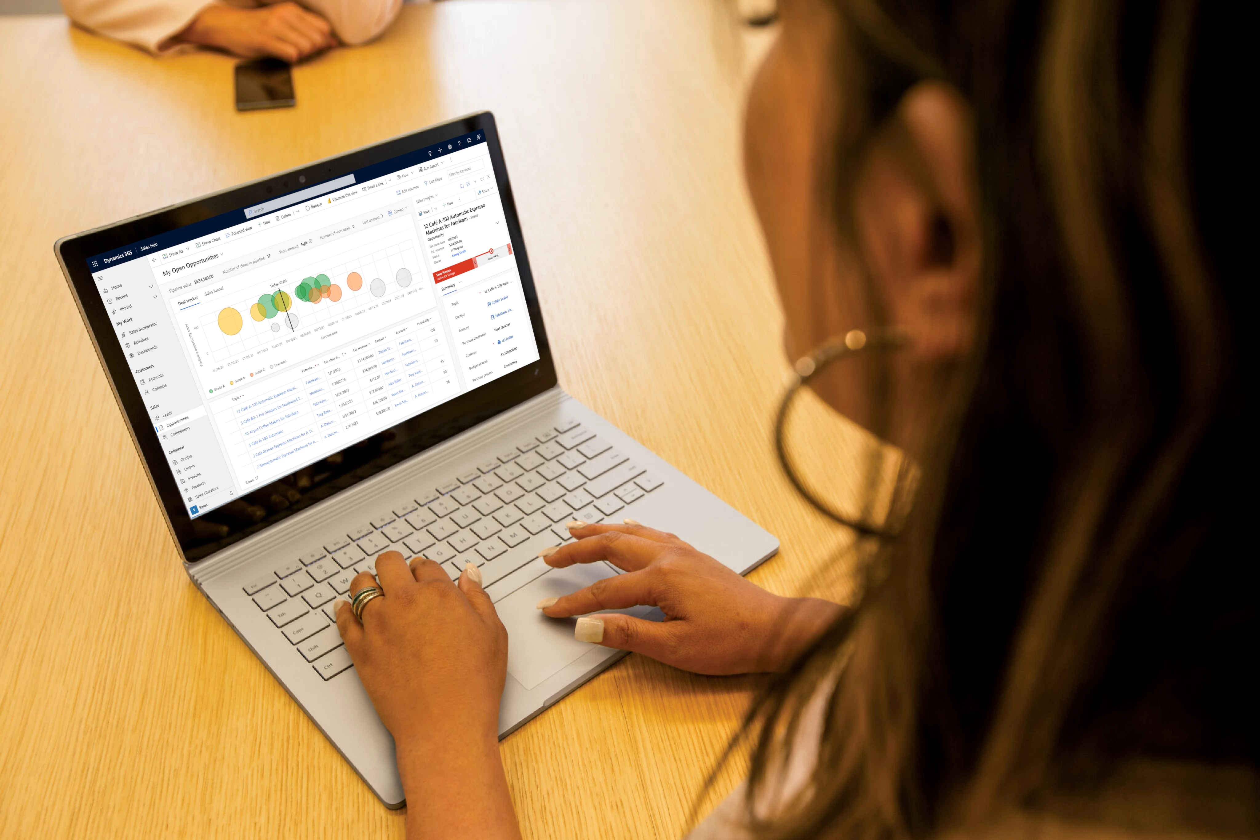 a person using a laptop computer sitting on top of a table, the laptop is showing the Dynamics 365 Sales open opportunity dashboard