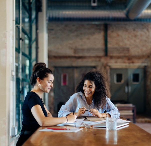 Two businesswomen talking at conference table in loft office.