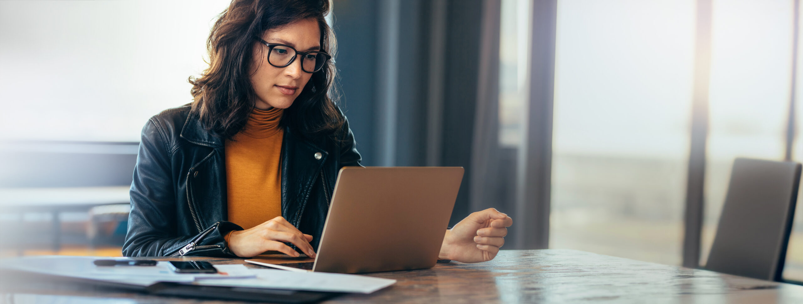 Asian business woman sitting at a table in an office, typing on her laptop with focus. Young female professional showing a dedication and commitment to her project at work.