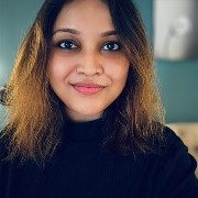 person wearing a dark top with shoulder‑length hair, indoors against a softly lit background