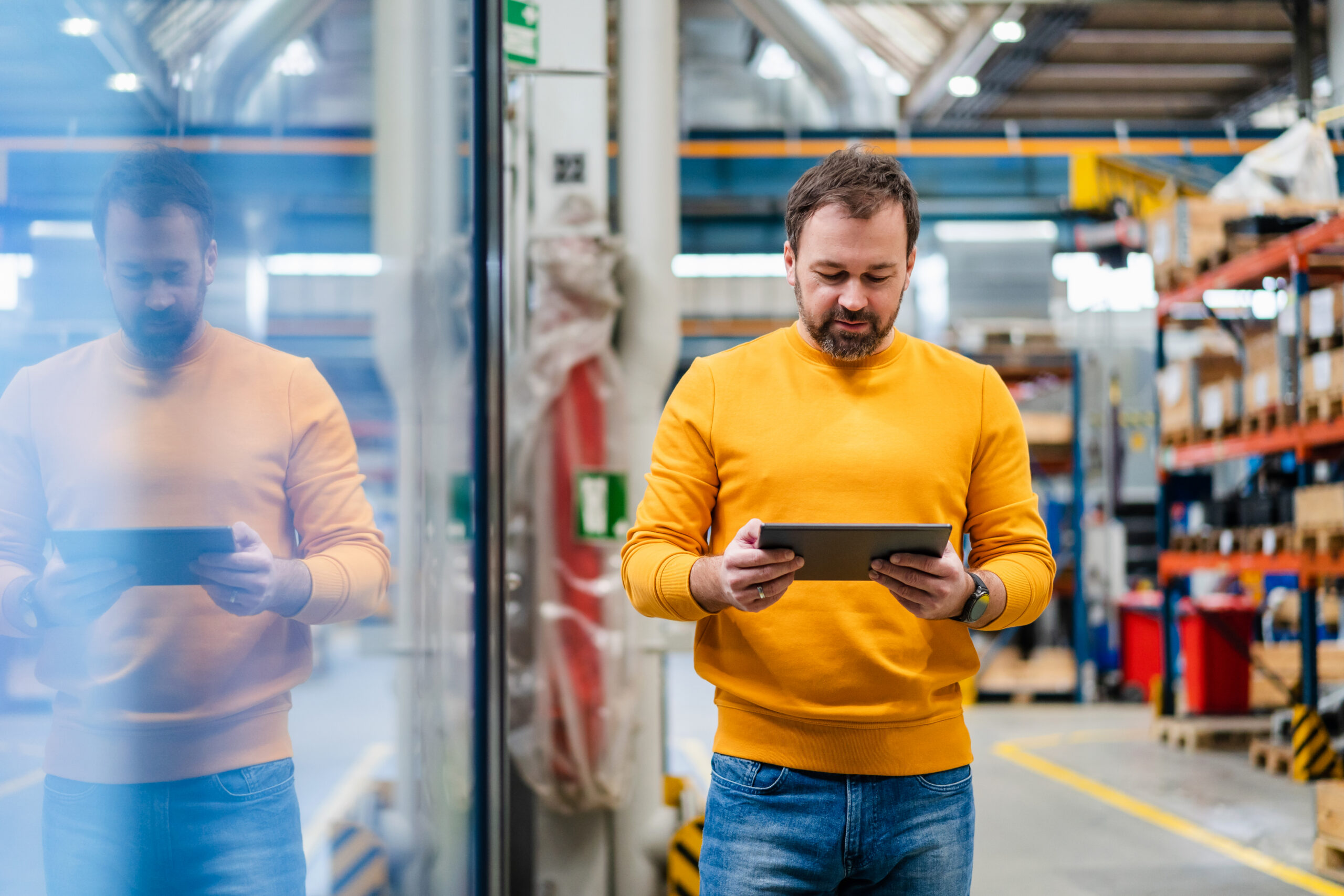 Person reviewing information on a tablet while standing on a warehouse floor with storage shelves in the background.