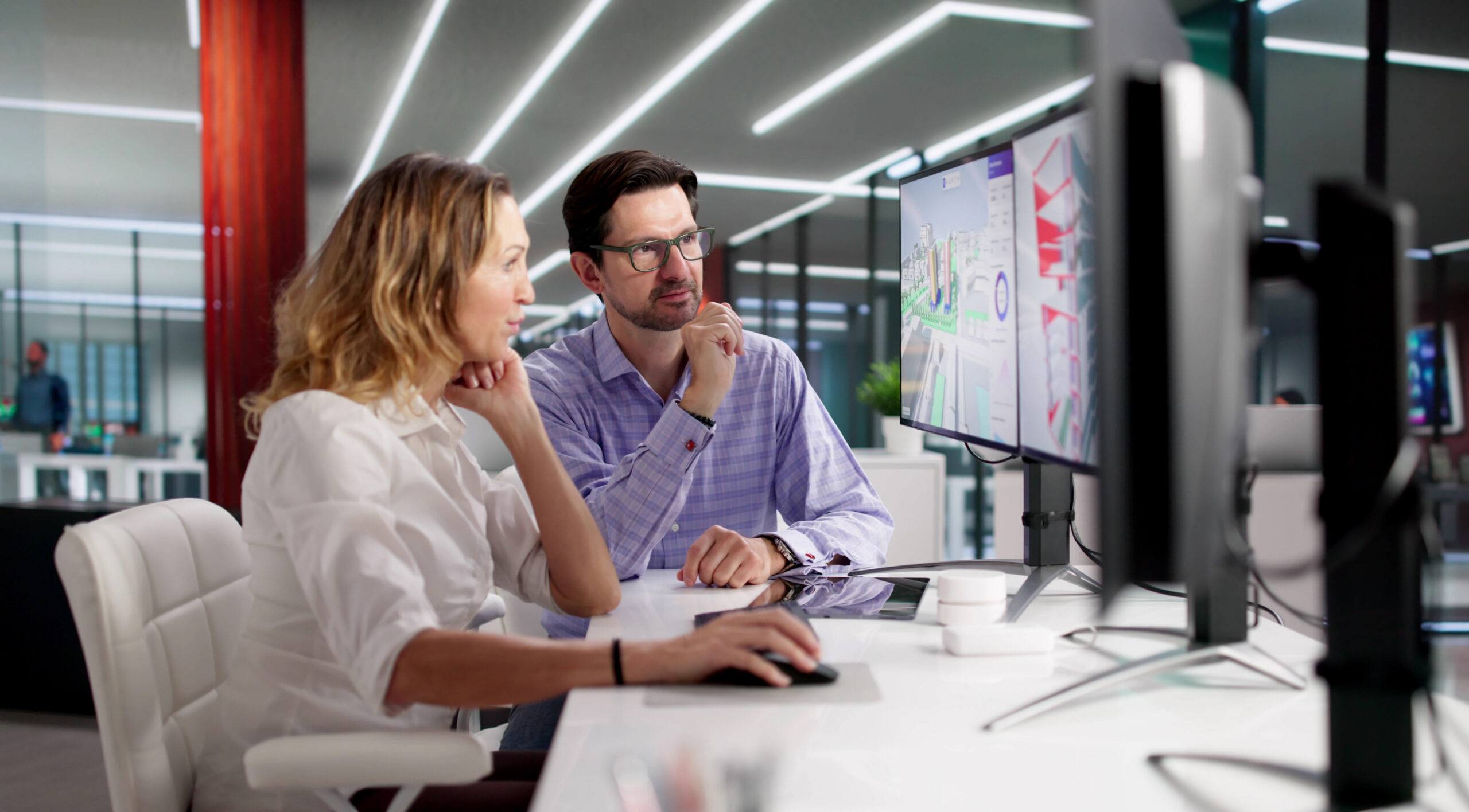 Two coworkers looking at shared screens and multiple monitors