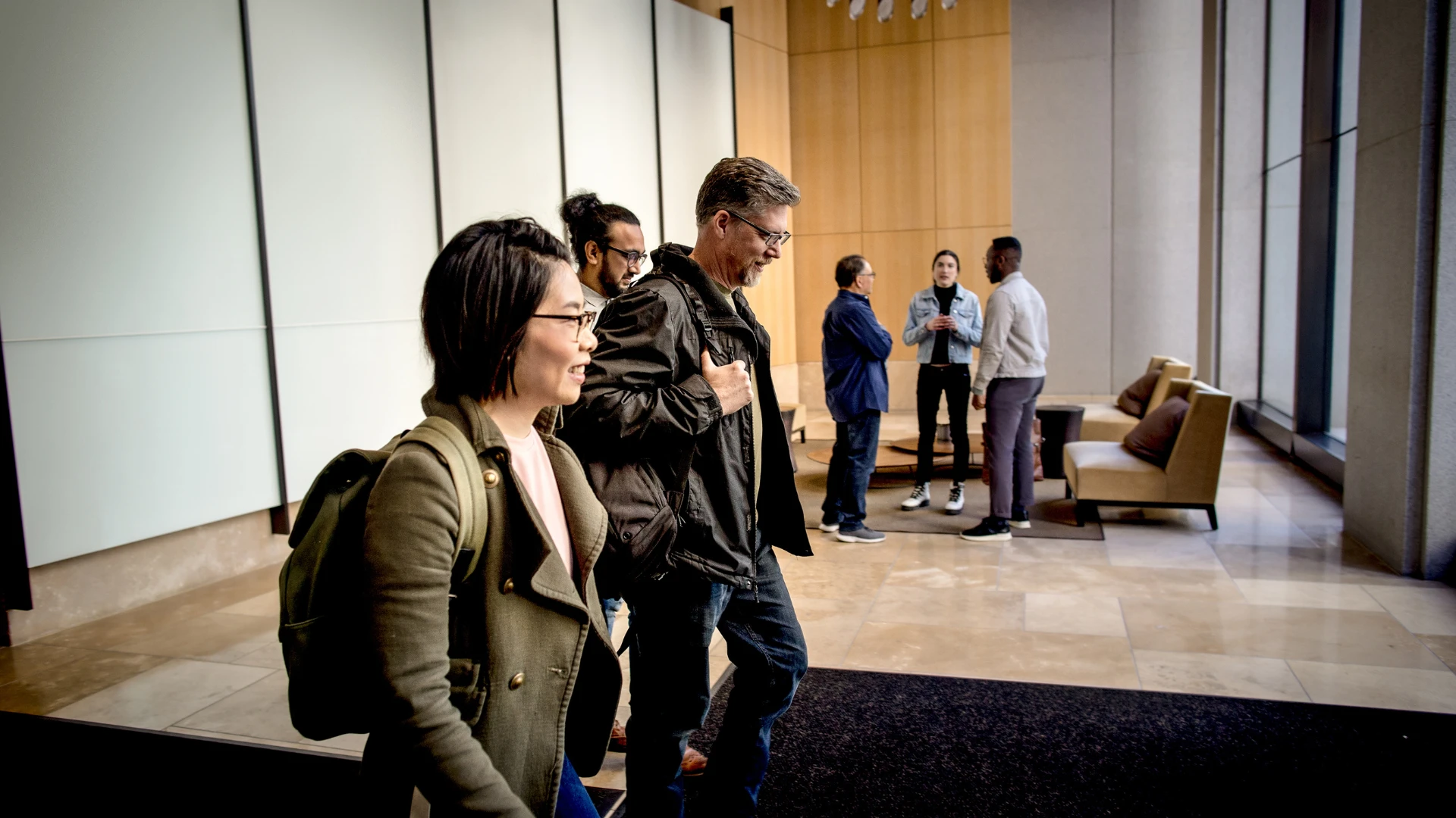 Employees walking through a modern office lobby while colleagues gather for a team discussion, representing workplace collaboration, customer relationship management (CRM) sales teams, and business productivity.