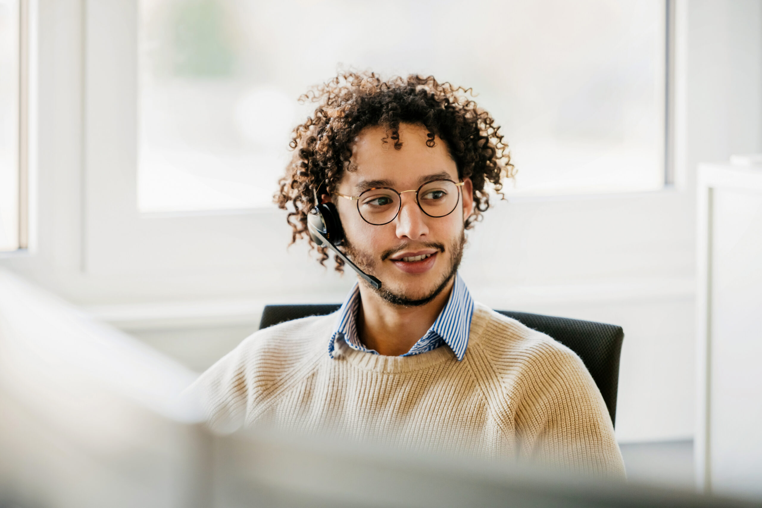 Person wearing glasses and a headset while working at a computer in a bright office