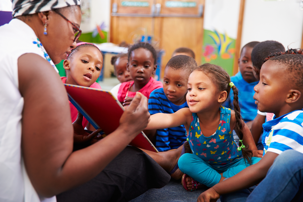 A teacher reading a book aloud to a group of young students in a classroom.