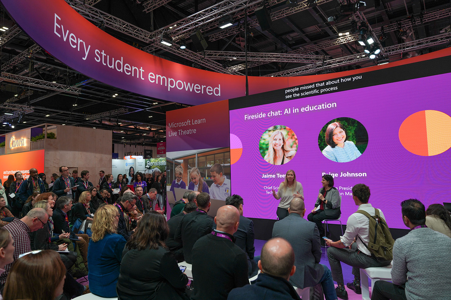 Two conference presenters speaking in front of a crowd of attendees in a large conference hall.