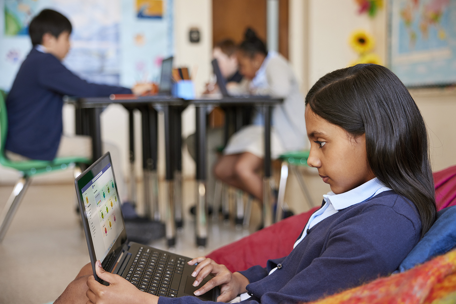 A student looking at their check-in responses in Microsoft Reflect on a laptop, while other students work at their desks in the background.