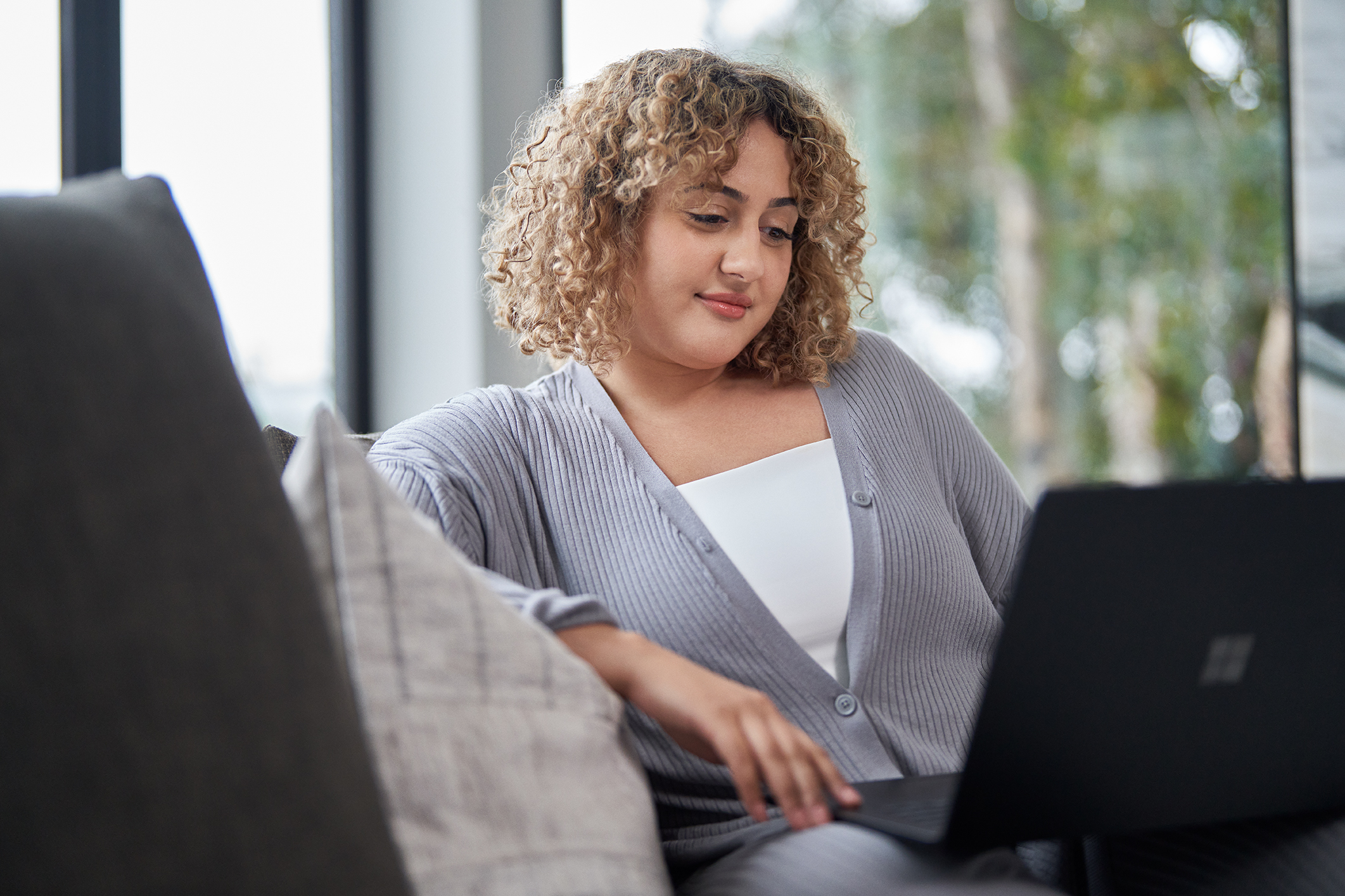 An educator sits on a sofa while looking at a laptop screen.