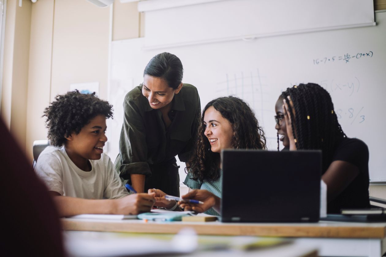 Happy educator talking with junior high students in classroom at school.
