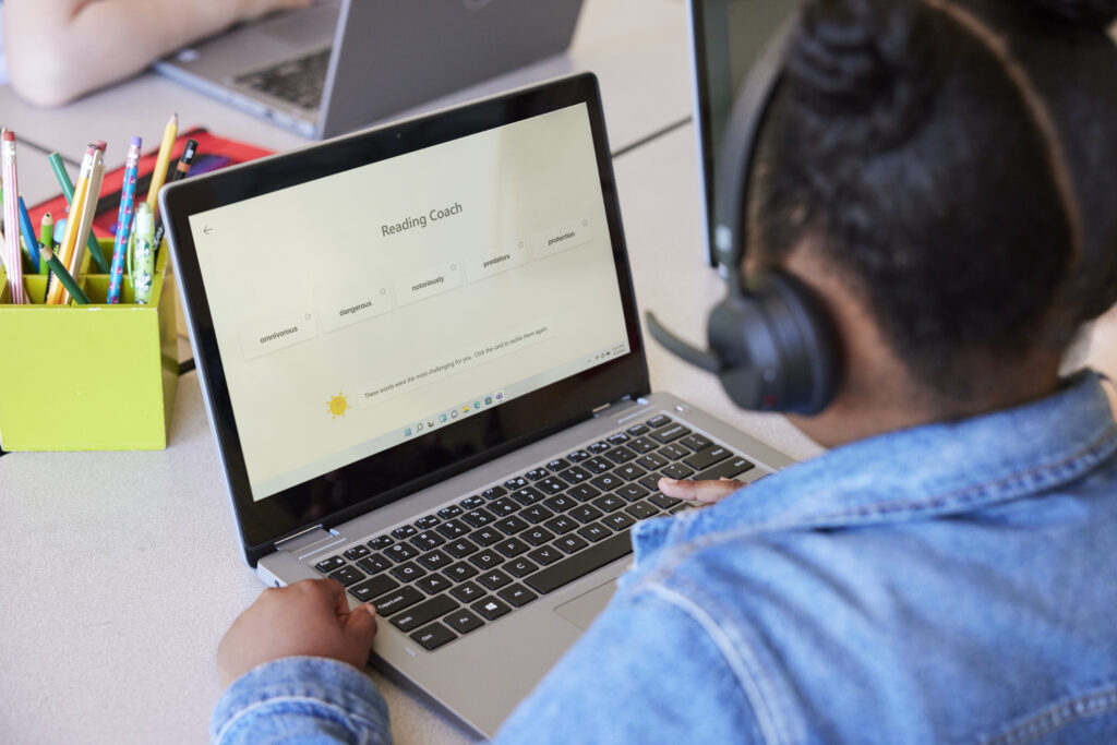 An elementary school student using Reading Coach on a laptop in a classroom setting, wearing headphones. 