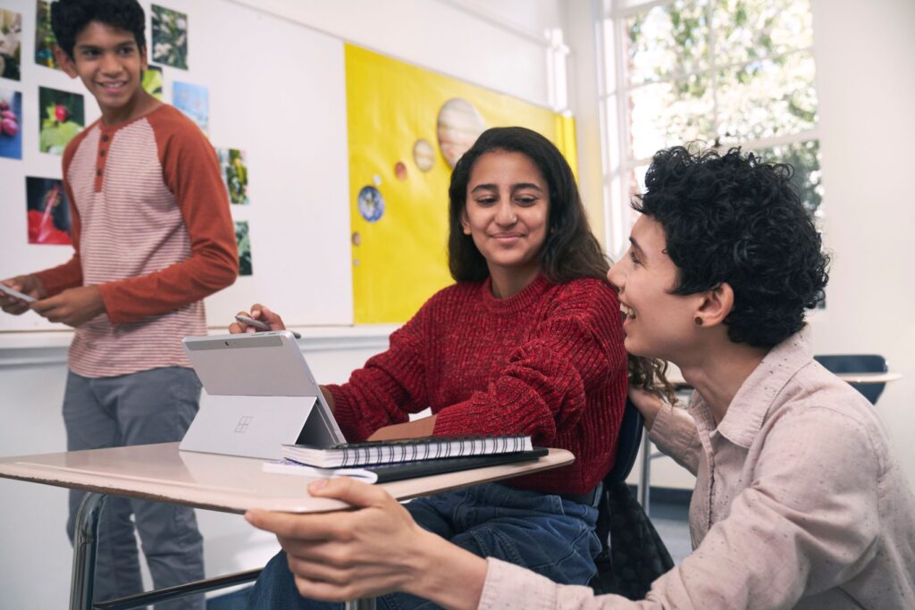 An educator engaging with two students in a school classroom.