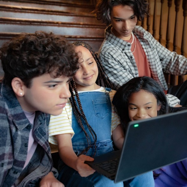 Four students sitting on a flight of stairs at school and looking at the screen of a laptop together.