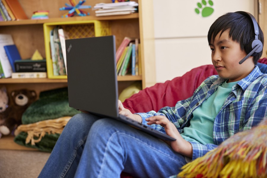 A student wearing headphones in a classroom setting and working independently on a laptop.
