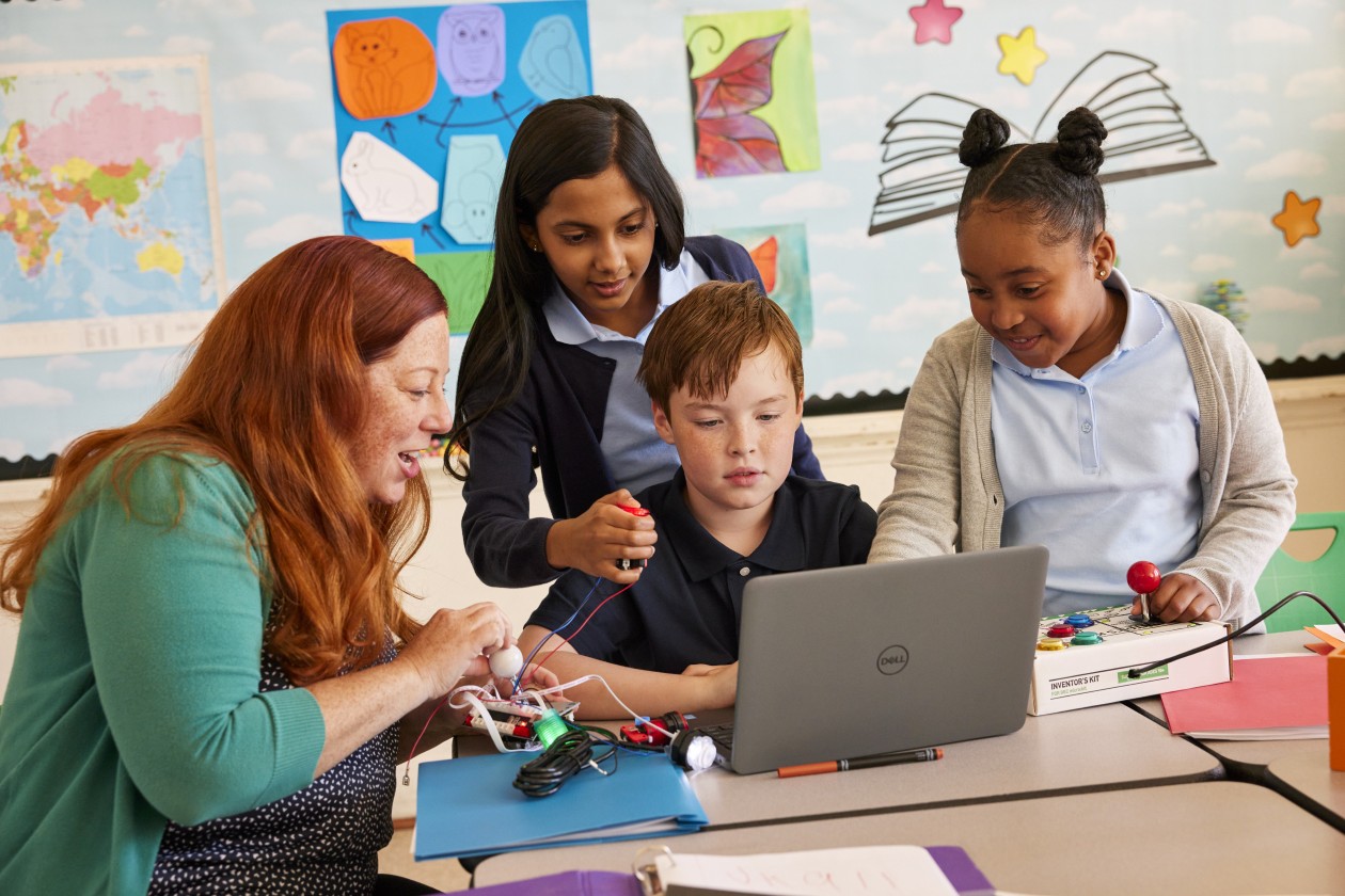 An educator engages with three students in a school classroom.