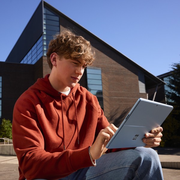 A student works on a 2-in-1 device while sitting outside a university building.