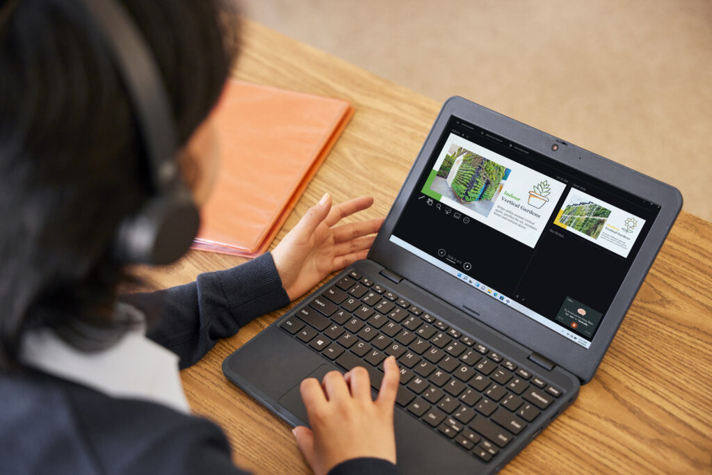 A student working on a laptop at their desk in a classroom. 