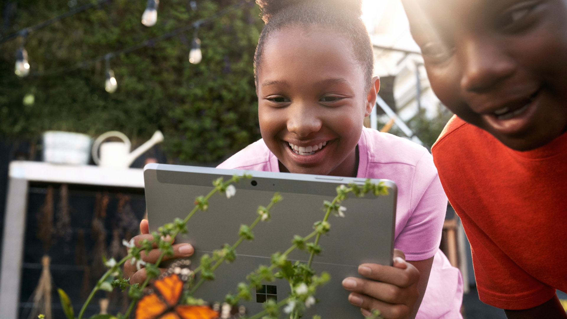 Two children engaged, looking at a tablet while outdoors in a grassy area