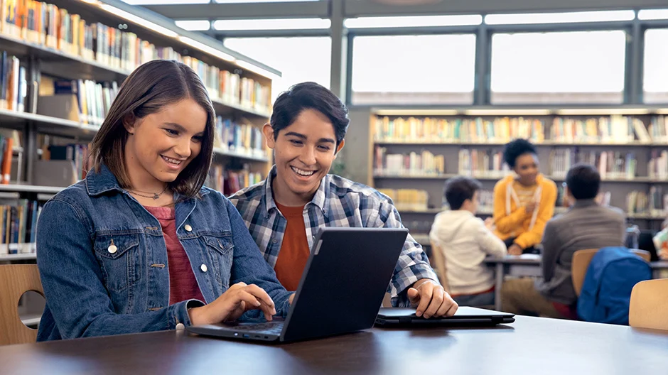 Two students working in a library looking at a laptop. 