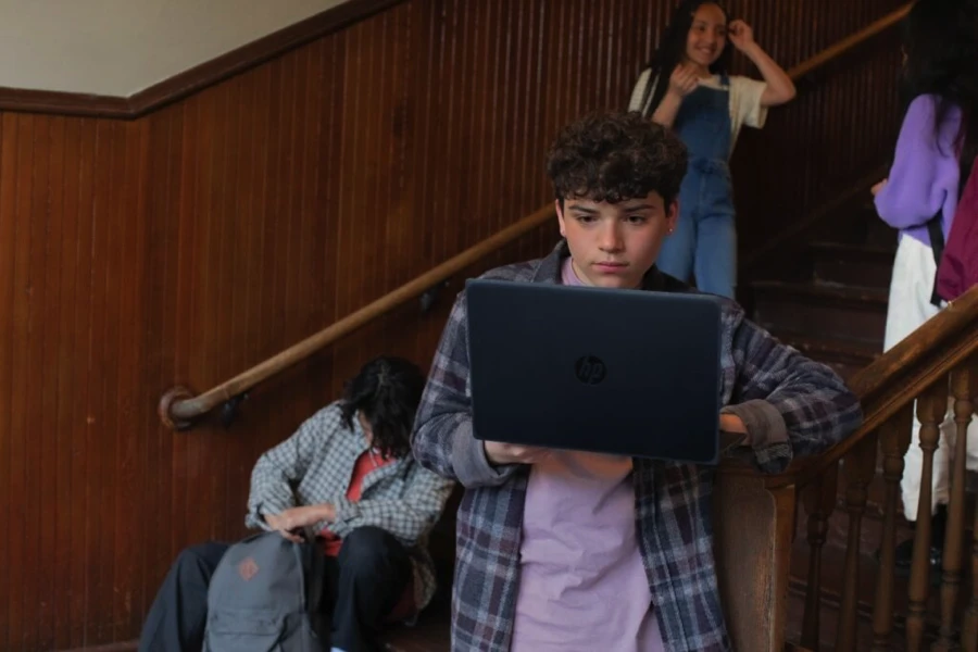 Decorative. A student holding a laptop next to a staircase with other students nearby.