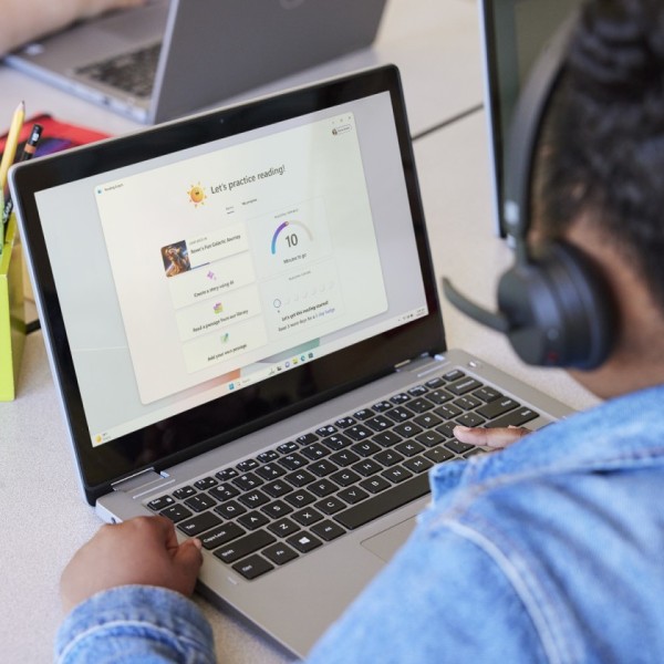 A student wearing headphones engages with Reading Coach while sitting at a desk in a school classroom.