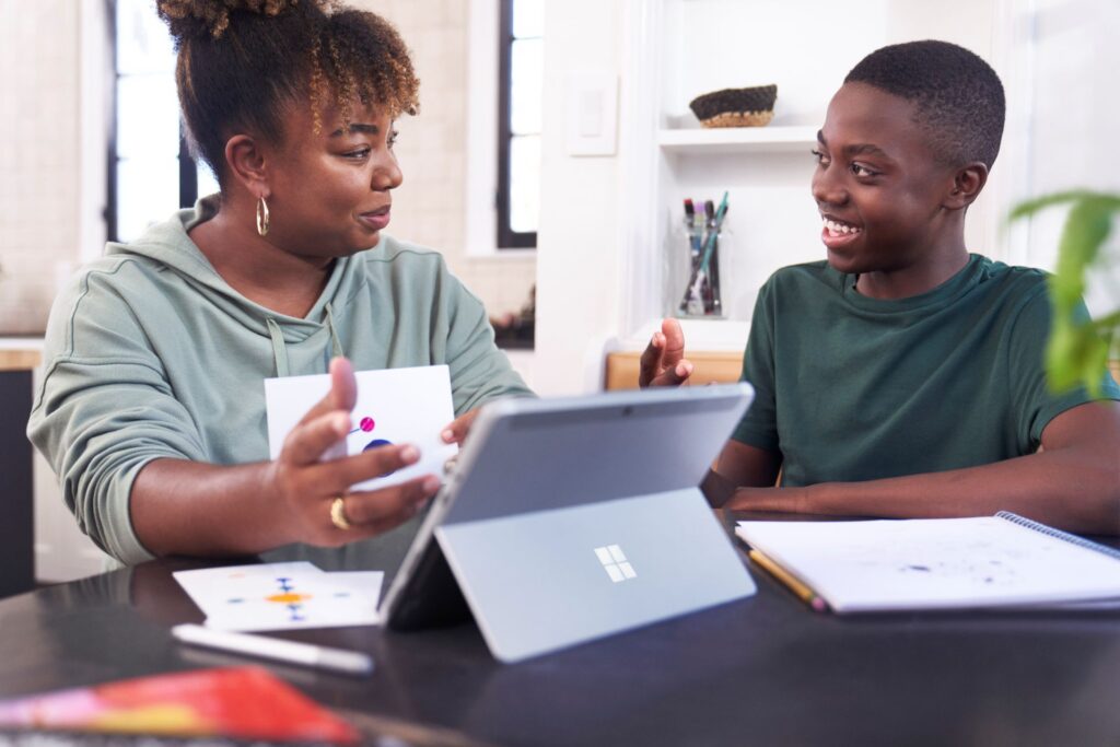 Woman teaching a boy at a table with a tablet and notebook