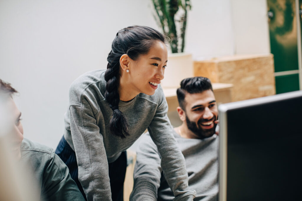 Smiling coworkers looking at computer while working in office