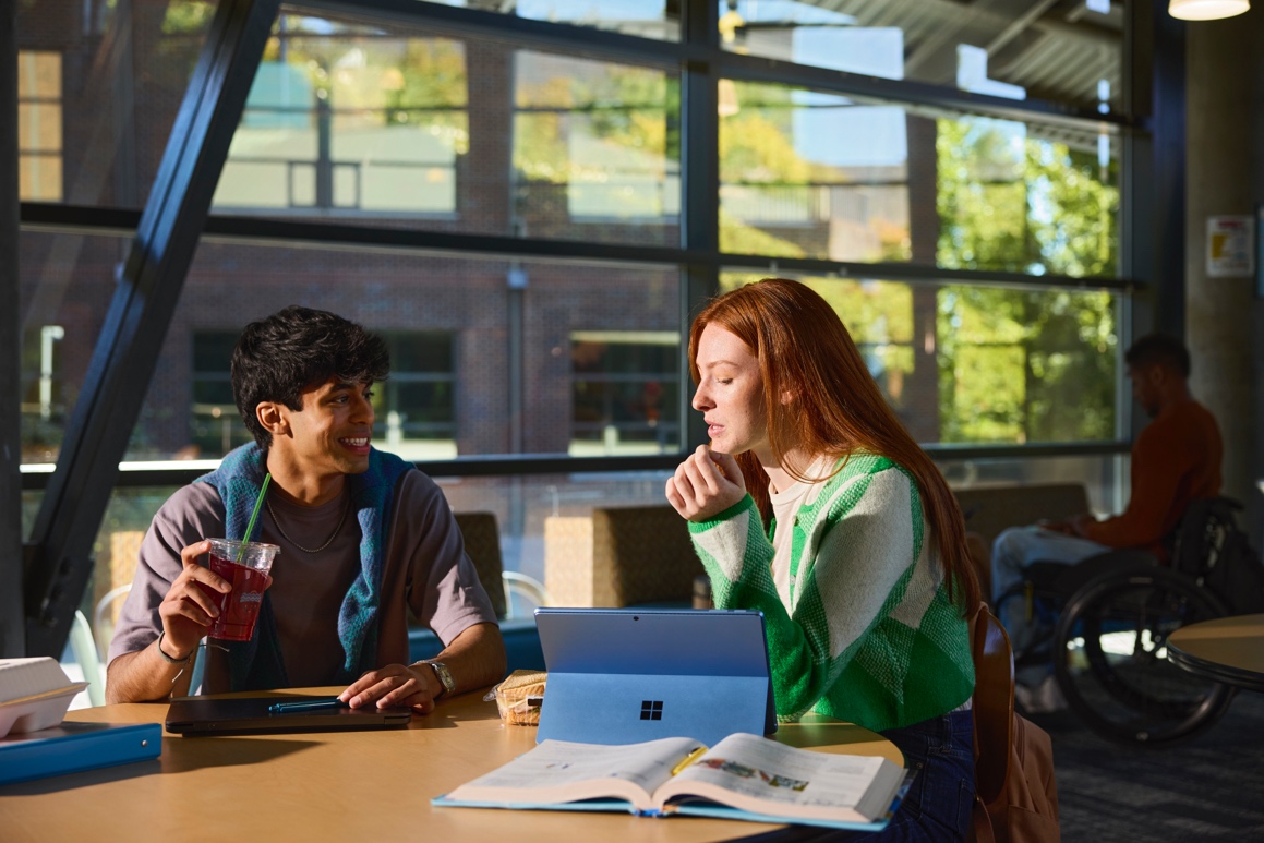 Two students sitting at a table and sharing a laptop.