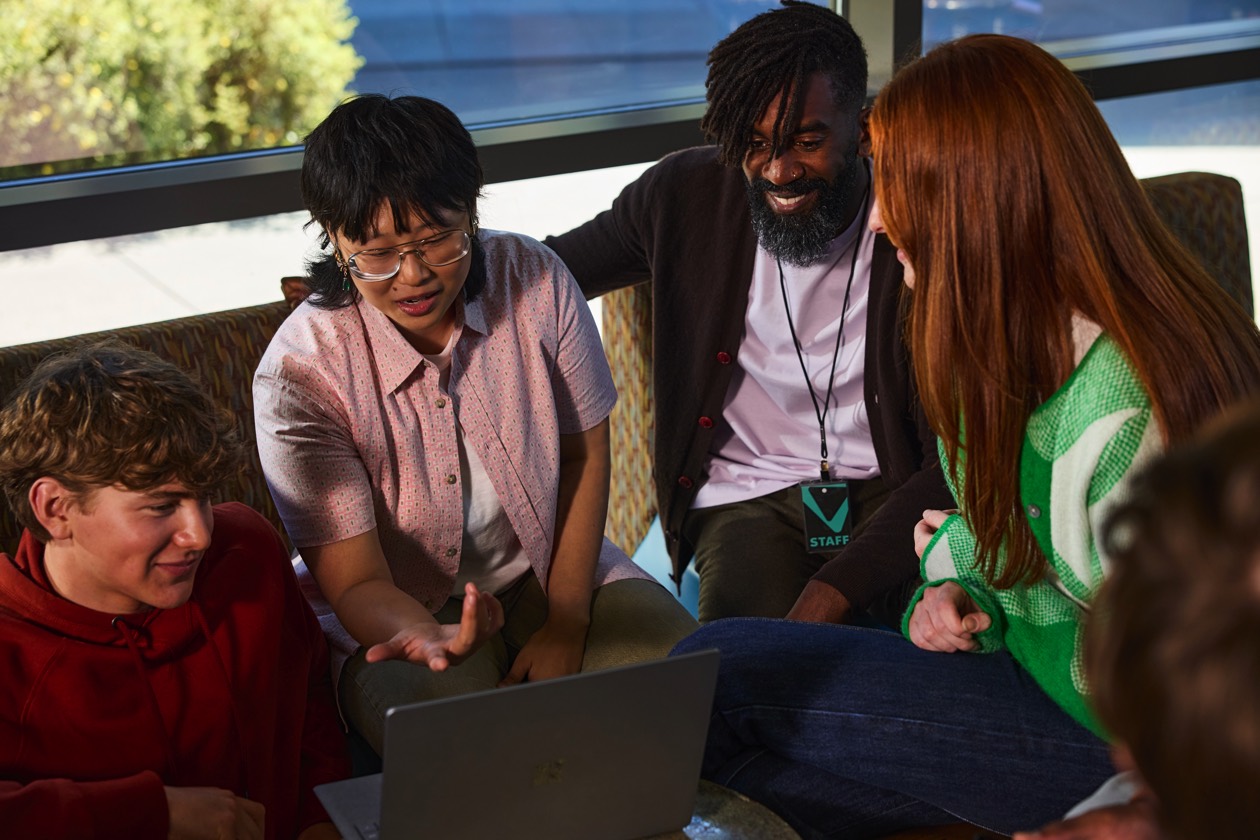 Students and teachers discussing classwork around a laptop.