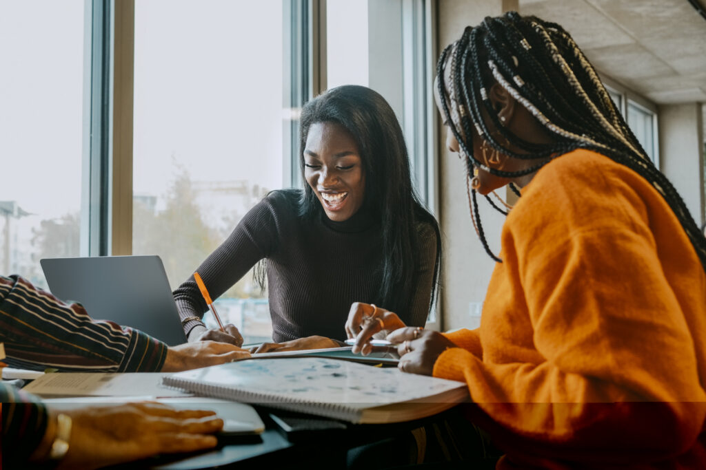 Cheerful female friends studying together while sitting at table in college cafeteria
