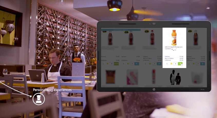 A picture of a man ordering groceries from a computer while sitting in a restaurant