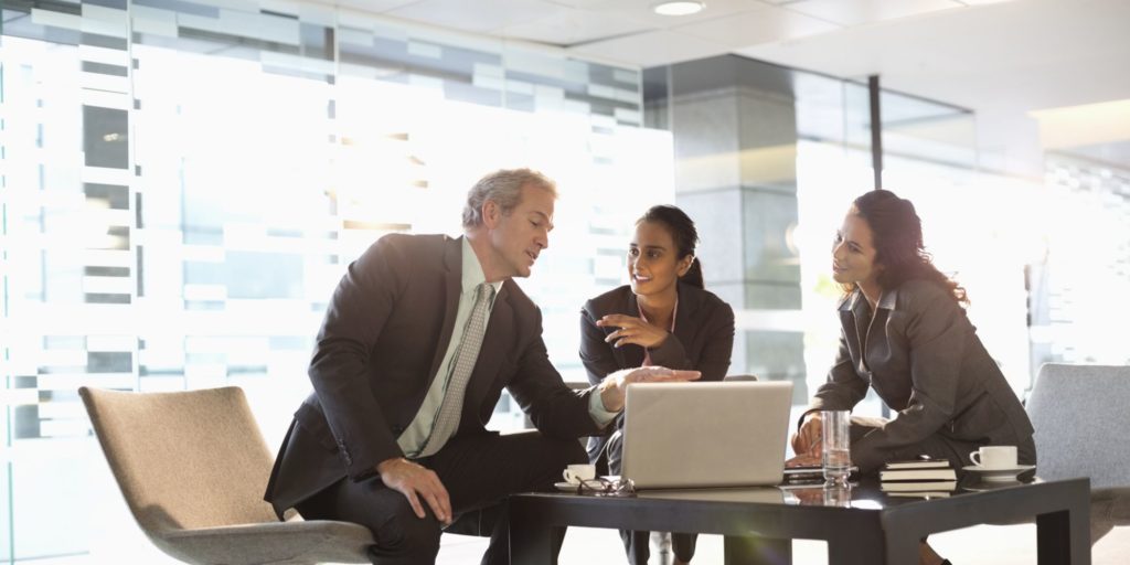 Three people discussing business while looking at laptop.