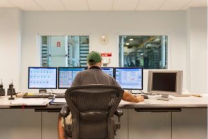 A man working at a desk with 5 computer monitors.
