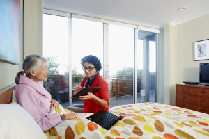 A caregiver showing a tablet screen to an elderly patient lying in a bed