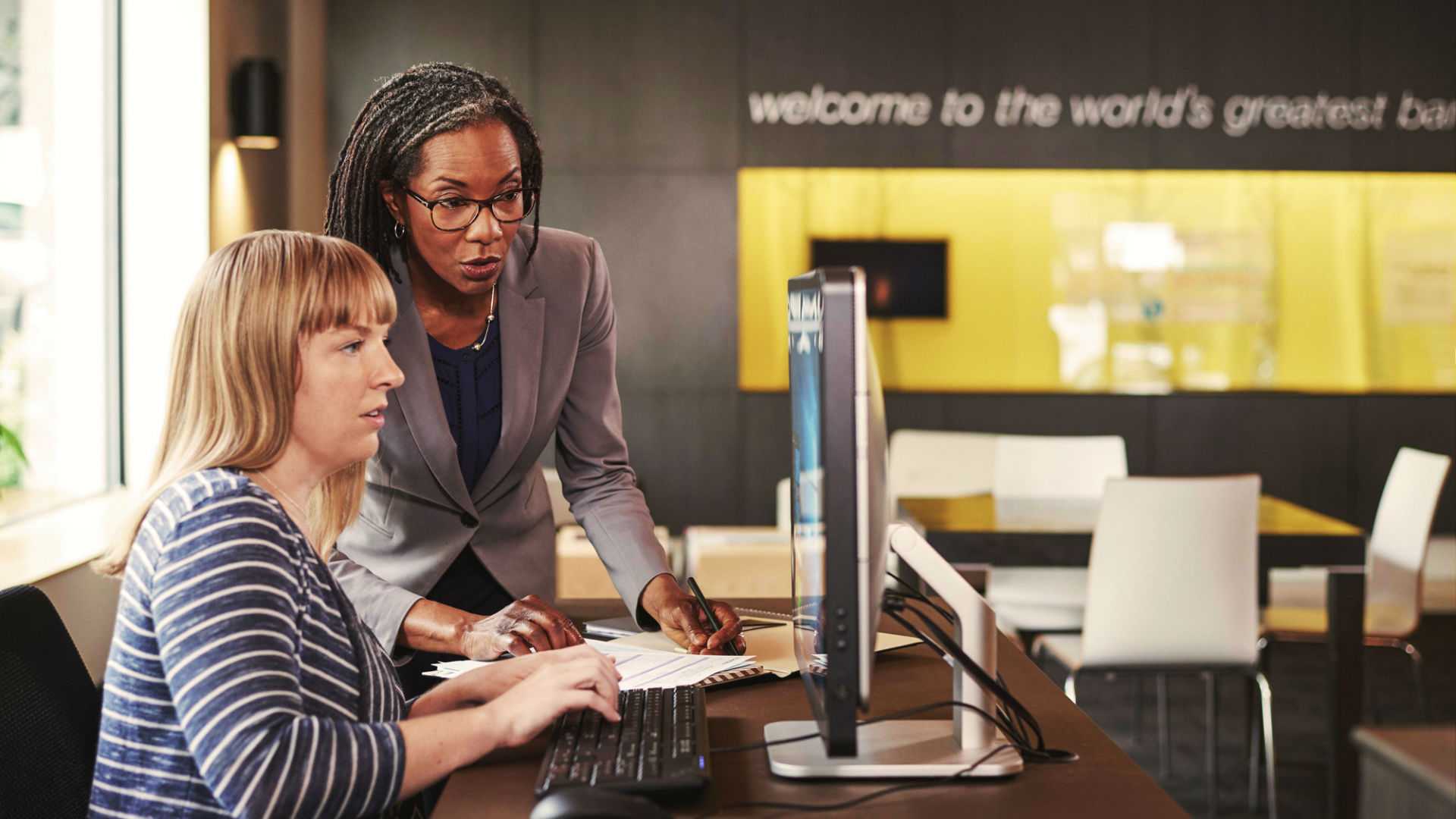 Two women working on a device in a bank