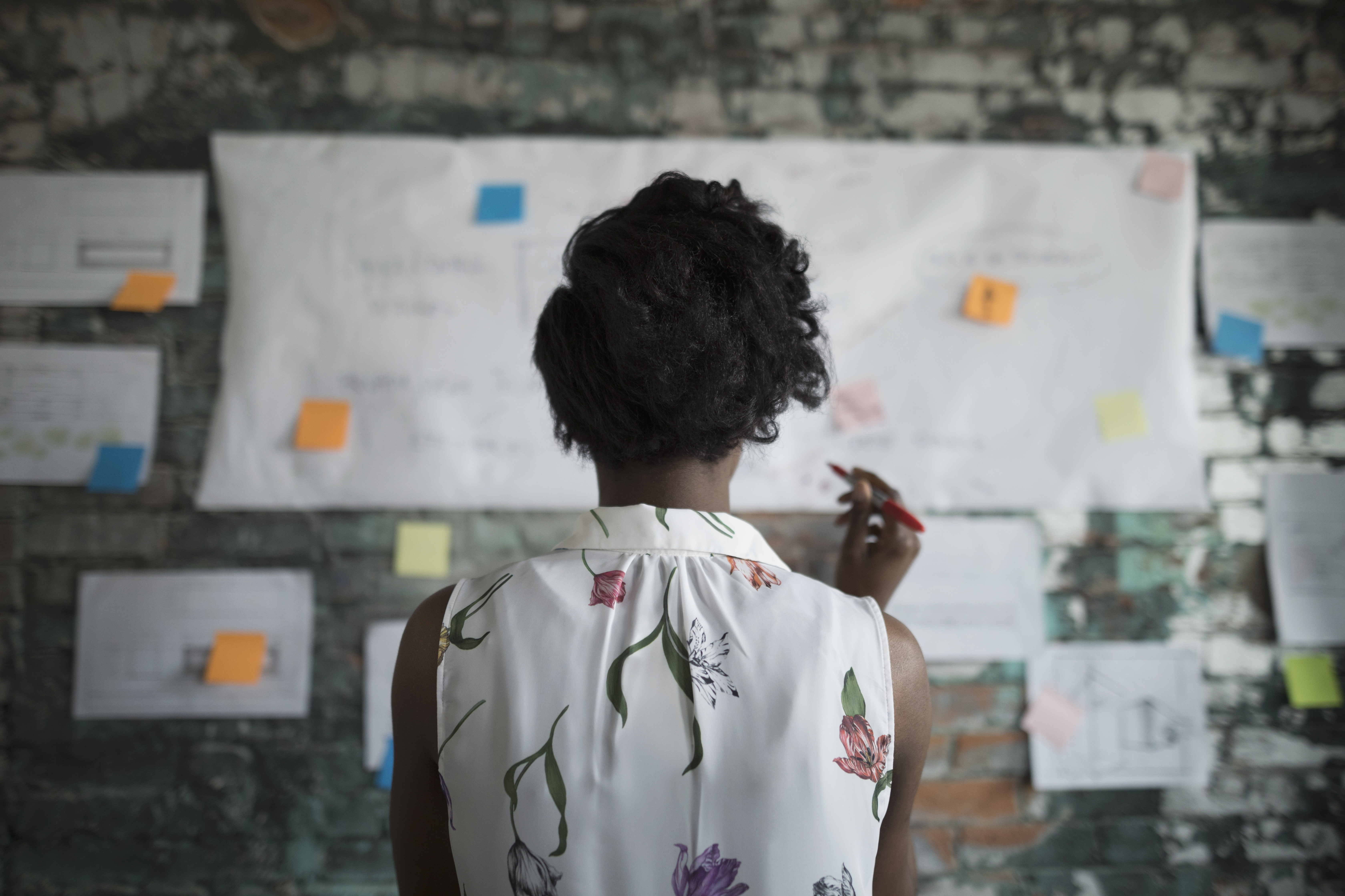 Businesswoman brainstorming, reviewing flow chart hanging on brick wall in office