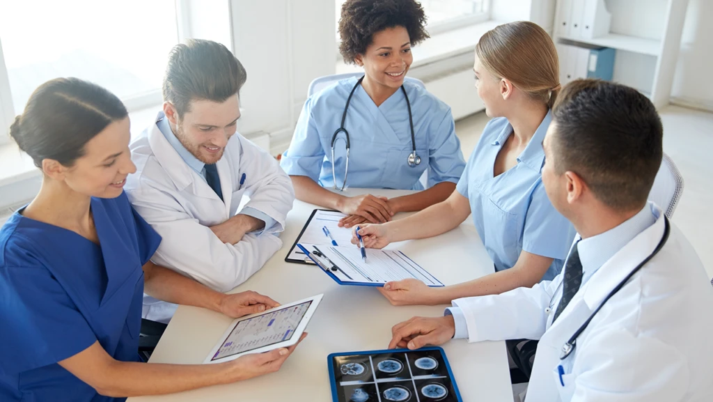 Health professionals sitting around a table looking at clipboards and tablets