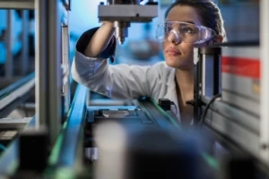 woman looking at a piece of machinery wearing safely goggles