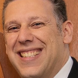 a man wearing a suit and tie smiling and looking at the camera