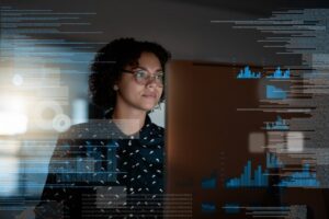 Shot of A person wearing glasses works at a computer screen. Images of data and charts overlay the image to infer what the person is working on at the computer console.