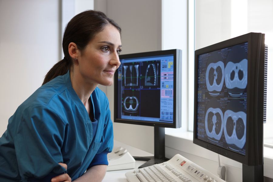 A woman in blue scrubs looking at computer screens