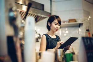 Portrait of a young female barista is using digital tablet in a coffee shop.