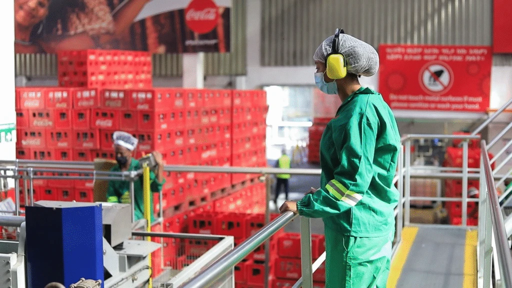 Coca-Cola Beverages Africa worker in personal protective equipment supervises warehouse operations.