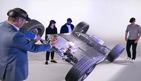 Four people are wearing HoloLenses and they are looking at a holographic car chassis