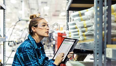 A woman who is standing in front of a shelf while she is holding a tablet PC